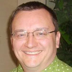 An image of Chris Lott, a white man with short brown hair, wearing a green shirt with white polka dots and glasses, and smiling at the camera