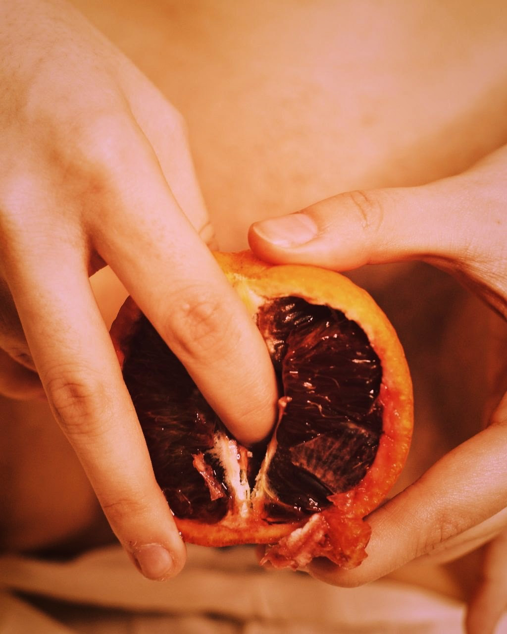 IMAGE: A hand inserts a finger into the open face of a halved fruit that has been placed in front of a person's pelvis.
