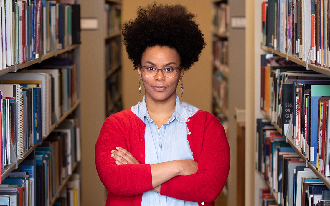 Teyanjulee Leon, '18, wearing red sweater, posing amid UW Tacoma Library book stacks