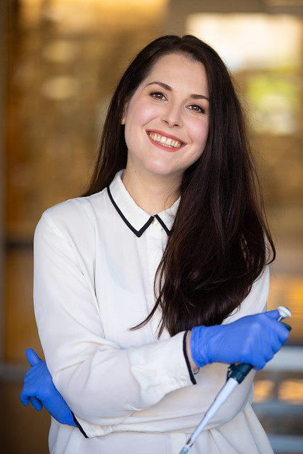 UW Tacoma alumna Emily Swanson, wearing blue lab gloves and holding a lab device