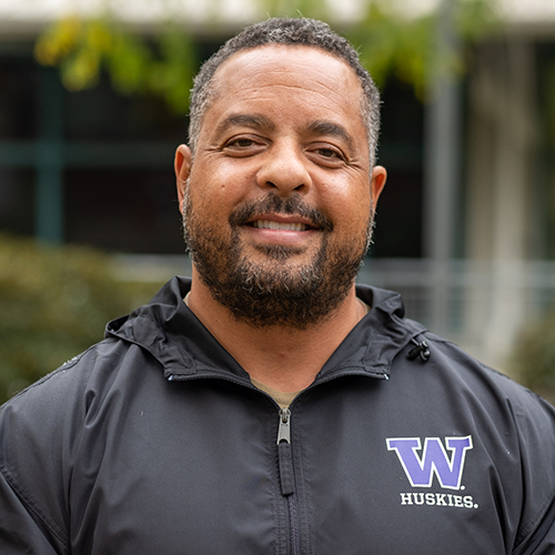 Headshot of UW Tacoma Educational Administration Program Director Kurt Hatch. There is a tree and green leaves in the background. He is wearing a black University of Washington rain jacket.