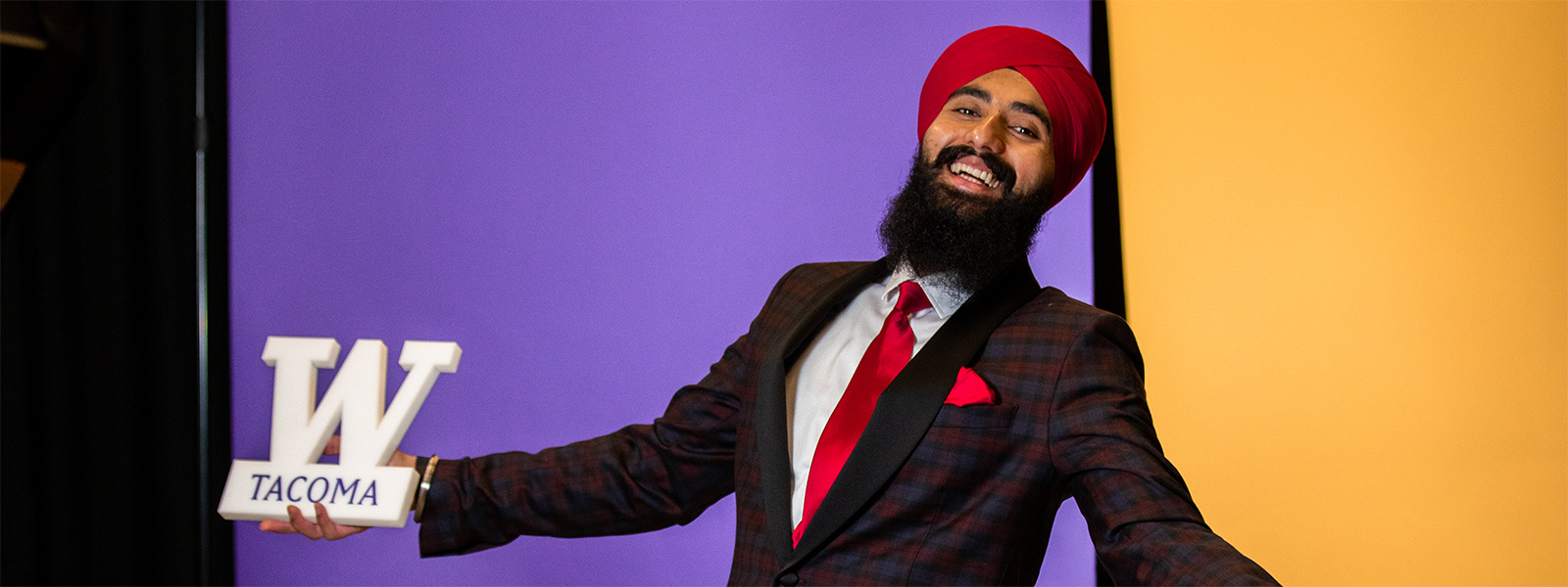 Gurchetan Singh holding a W Tacoma prop, with purple and gold screens in background