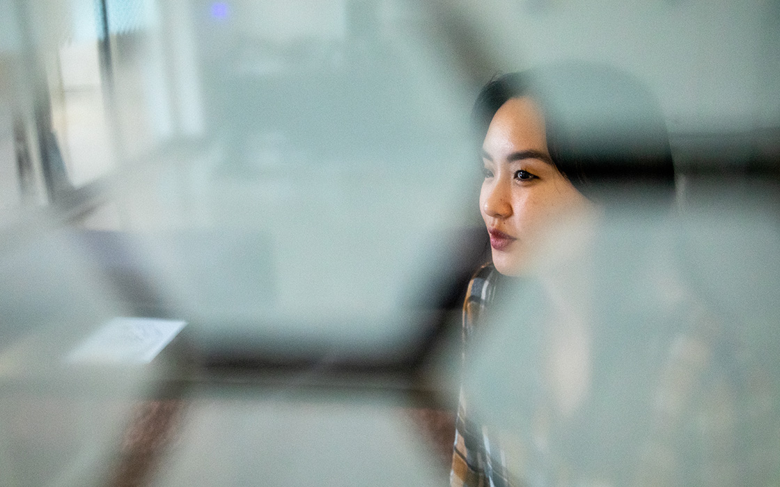UW Tacoma alumna Lan Allison looks out the window of the Global Innovation and Design Lab. Her face is partially obscured by an opaque, honeycomb shaped graphic on the glass.