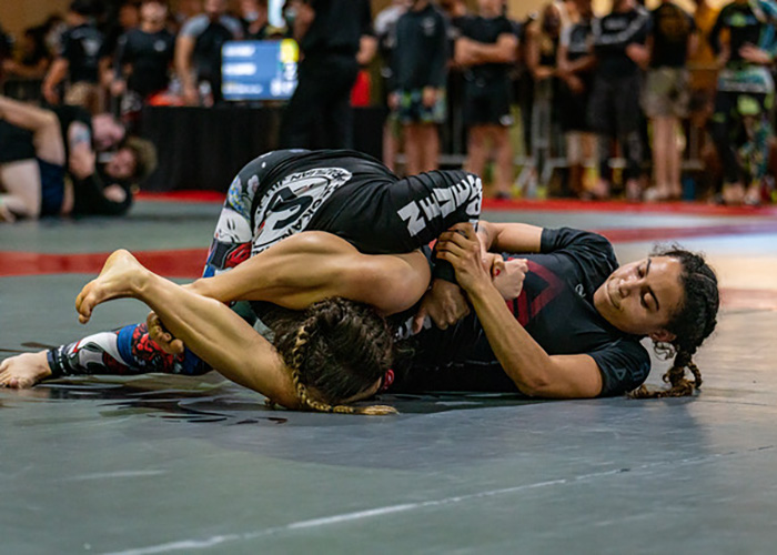 UW Tacoma alumna Saranda Ross wrestling with an unidentified individual for a martial arts tournament. Both are on the ground and Ross has holding the person's arm with her arms and has the other person's head between her legs.