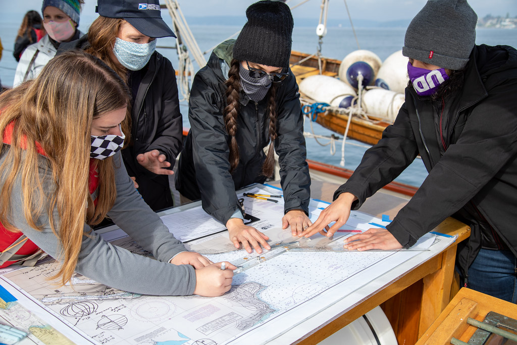 Students and alumni are instructed on reading a nautical chart aboard Adventuress, on Commencement Bay