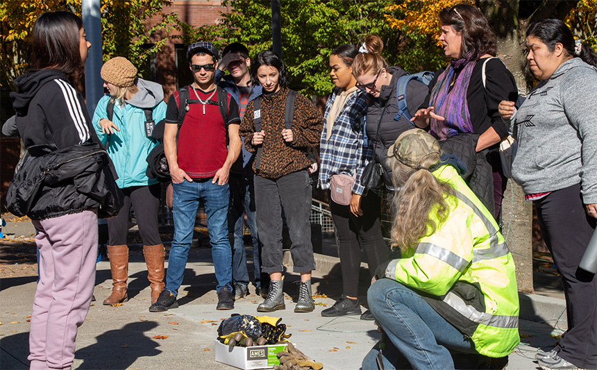 UW Tacoma students surround UW Tacoma head gardener Kim Bode, learning about tulip bulb planting.