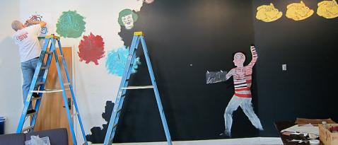Artist on ladder paints a wall mural.