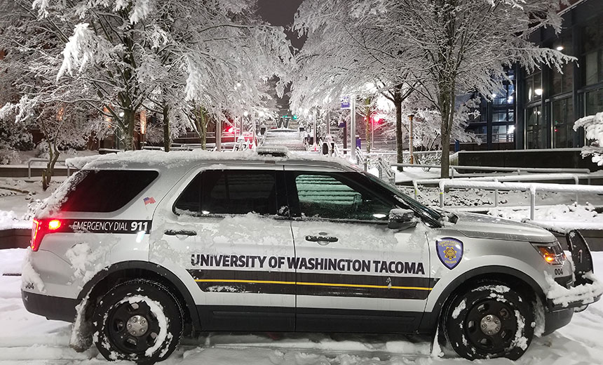 UW Tacoma campus safety car at night with snow-covered UW Tacoma campus in background.