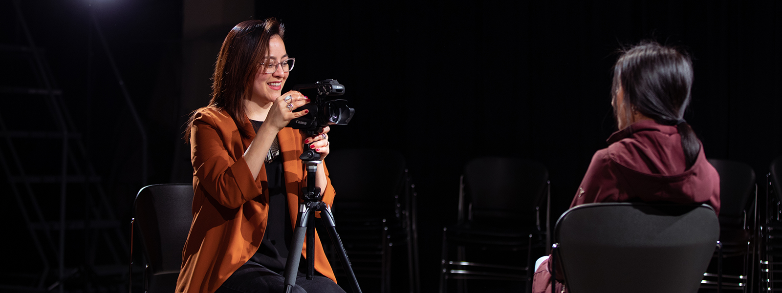 Dr. Sonia De La Cruz in a darkened studio focusing a camera on an interviewee.