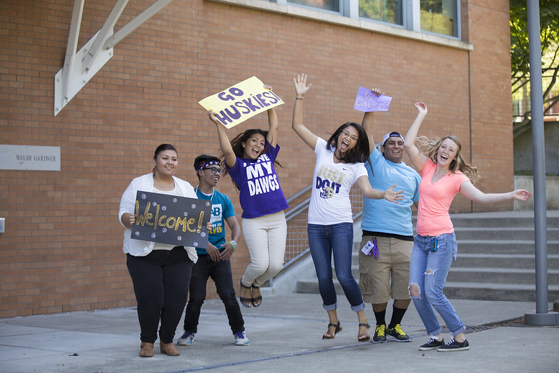 group of students jumping with "go huskies" and "welcome" signs 