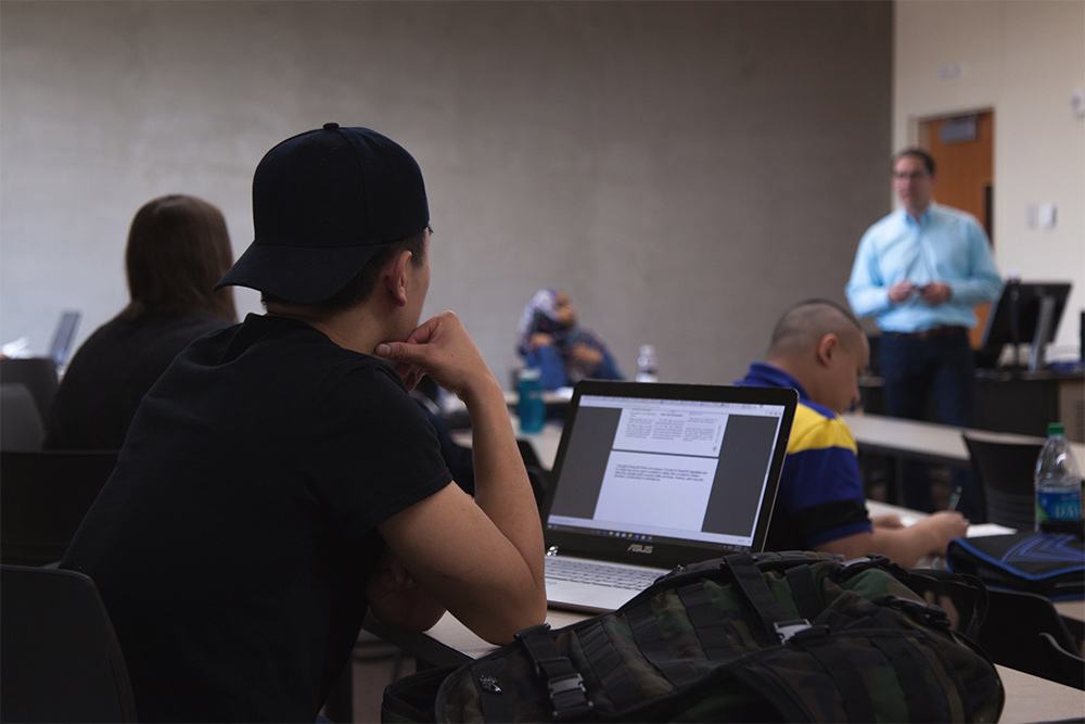 A student attends TMGMT 466 in spring 2017, taught by Joe Lawless, seen in background.