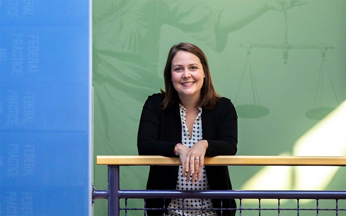 UW Tacoma Assistant Professor Sarah Hampson posed in front of green wall with supergraphic of allegorical figure holding scales of justice.