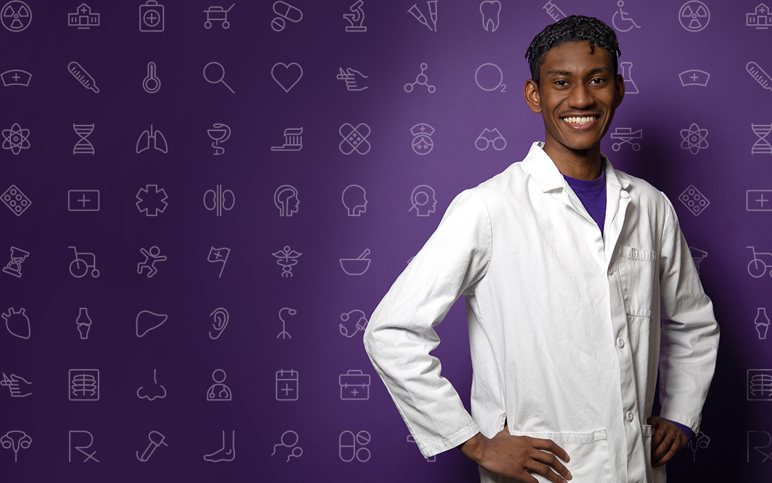 UW Tacoma junior Christian James stands on the right side of the photo. He is wearing a white lab coat with a purple shirt underneath. His hands are on his hips. There is a purple background behind him with various medical symbols on it.
