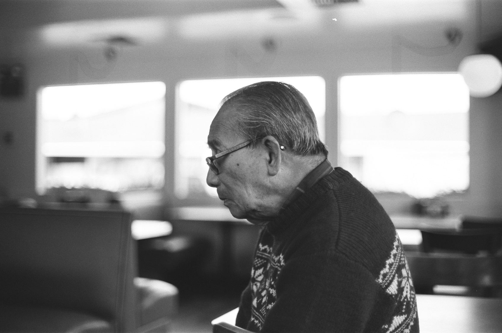 PICTURED: A black and white portrait of the photographer's grandfather in profile. Restaurant booth seating is in the background.