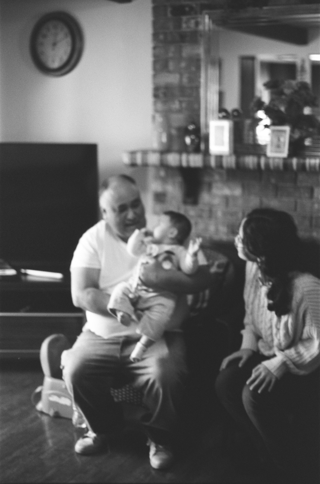 PICTURED: A black and white photo of one adult holding a baby while another watches.