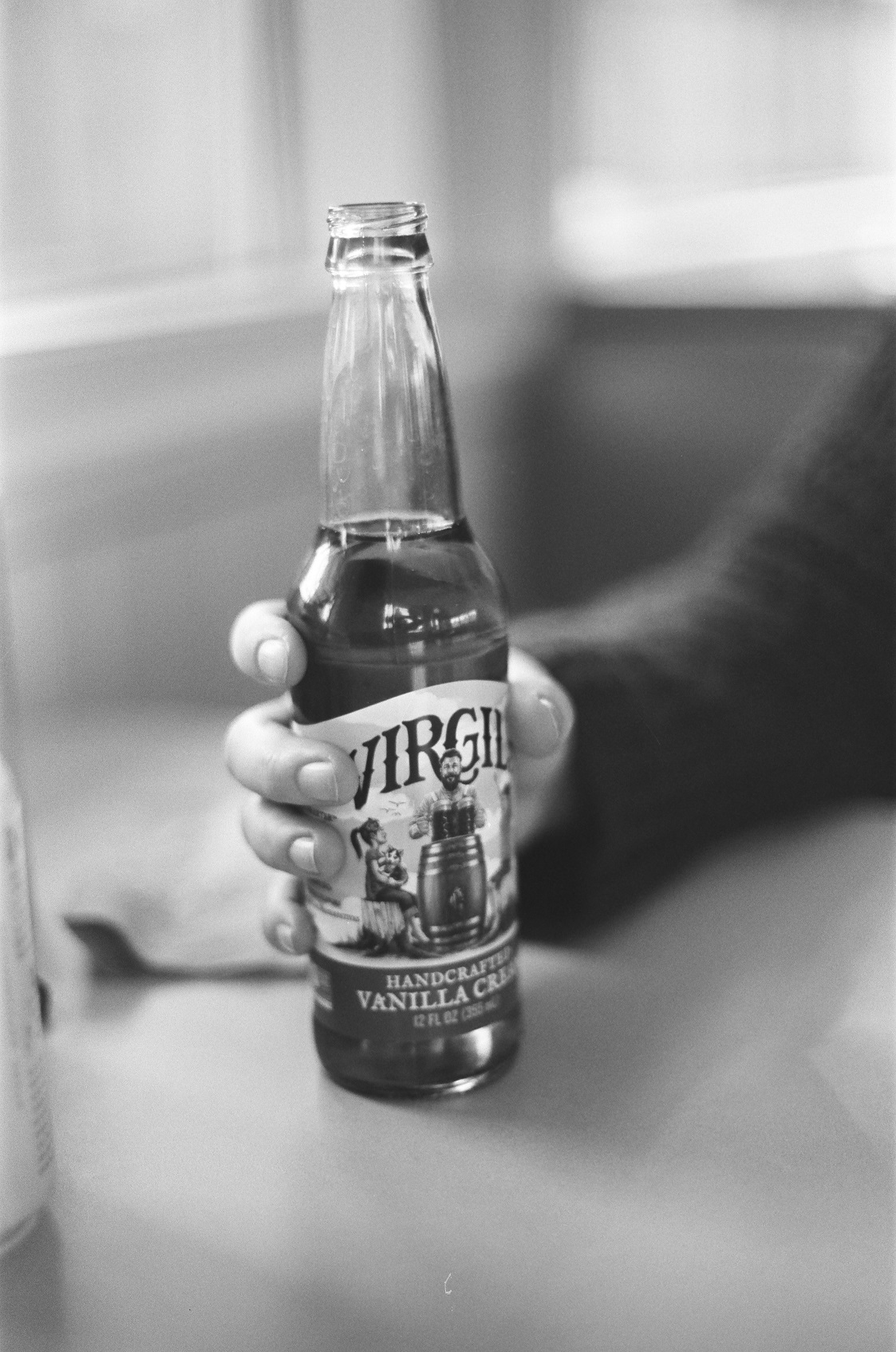 PICTURED: A black and white photo of a hand holding a glass bottle of soda pop.