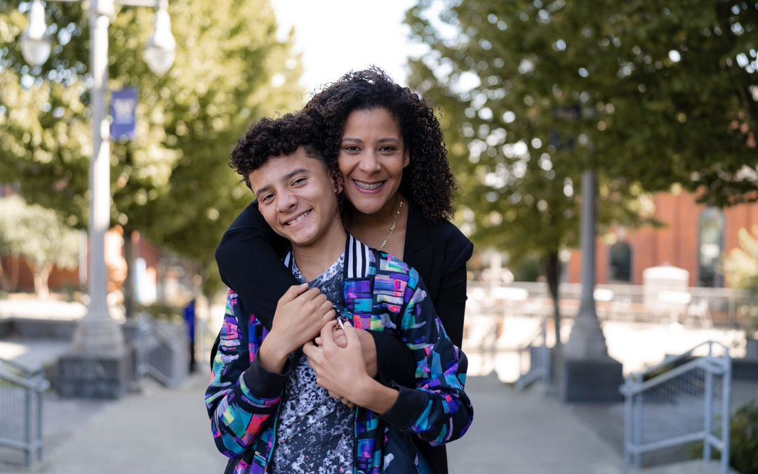 UW Tacoma alumna Alishia Agee-Cooper poses with her son on the Grand Staircase. Agee-Cooper is standing behind her son and has her arms over his shoulders. The pair are smiling and holding hands.