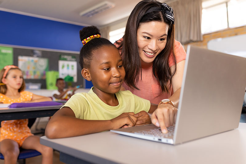 Teacher assisting students working on laptop in a classroom