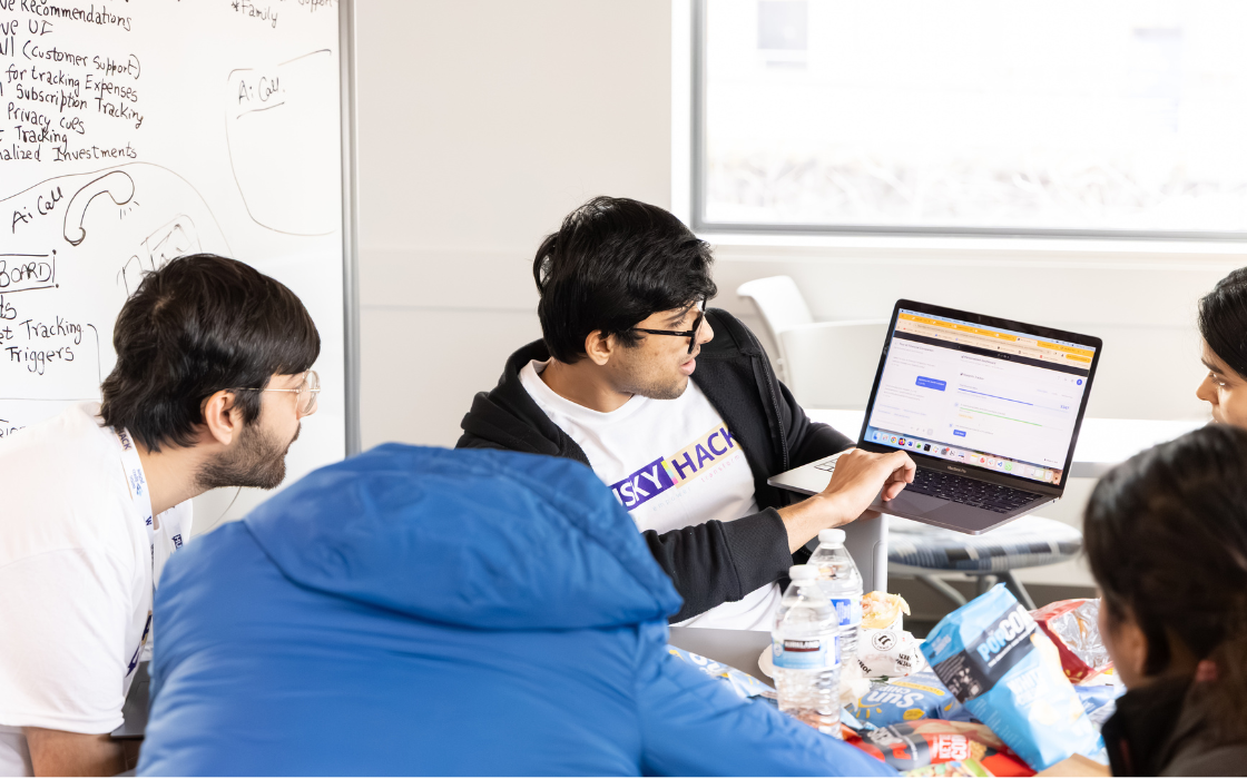 Five students gathered around a laptop, looking at the screen together.