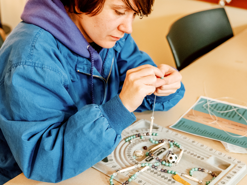 Student beading a long chain of blue beads with a soccer ball pendant in the Family Room