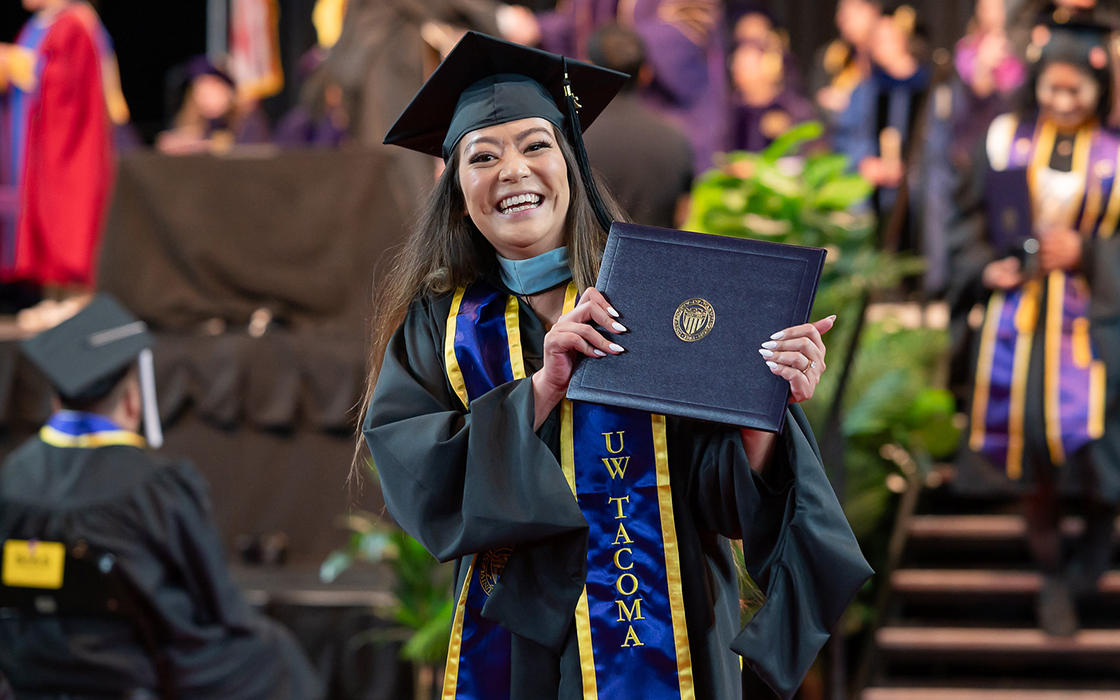A graduate holds up their diploma cover while smiling during UW Tacoma's 2025 commencement.