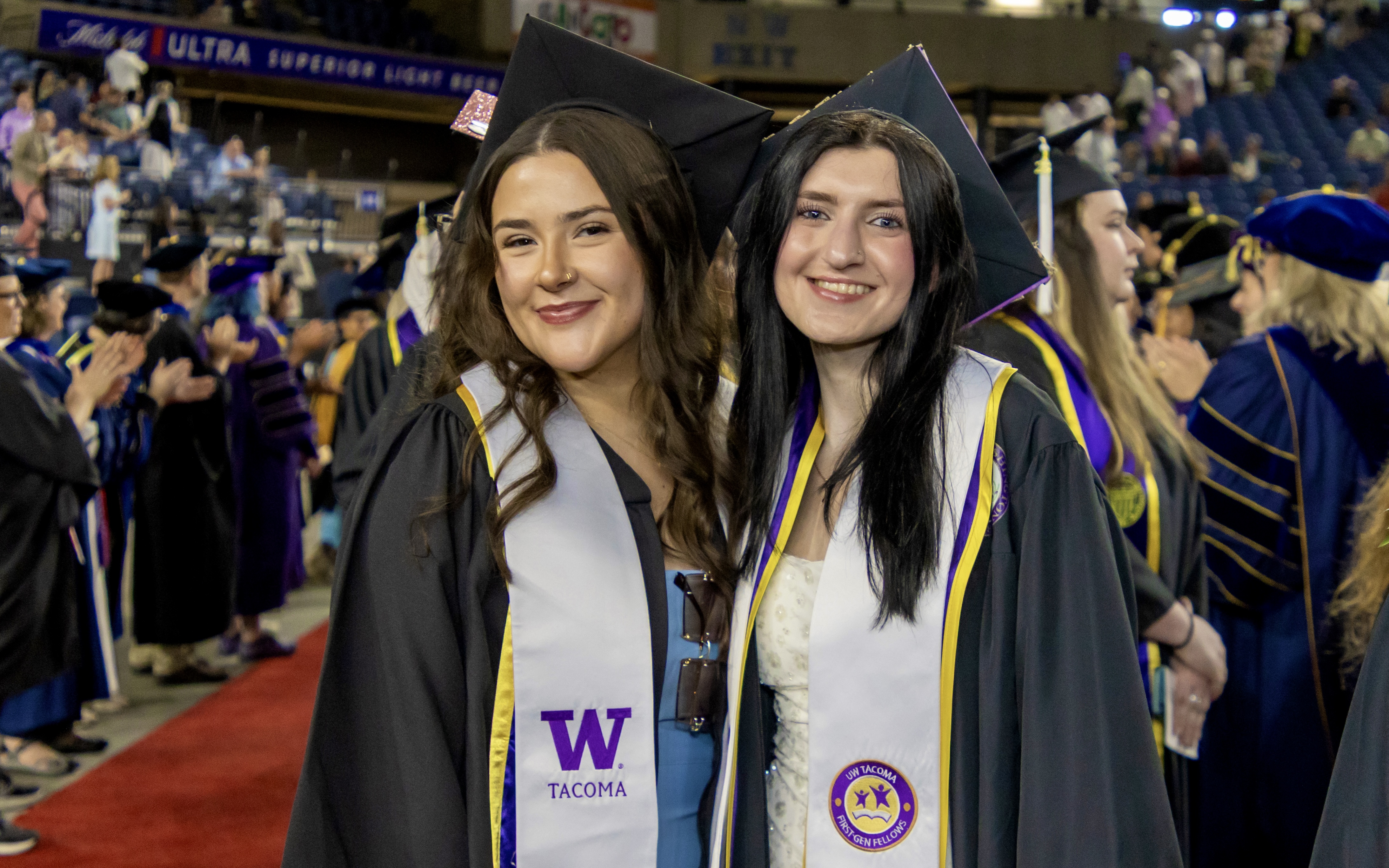 A photo of two UW Tacoma graduates smiling at the university's Commencement ceremony at the Tacoma Dome.