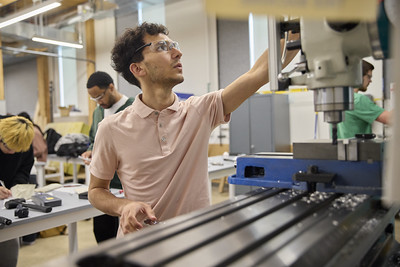 A UW Tacoma student adjusts a machine in an engineering lab, with other students working on hands-on projects in the background.