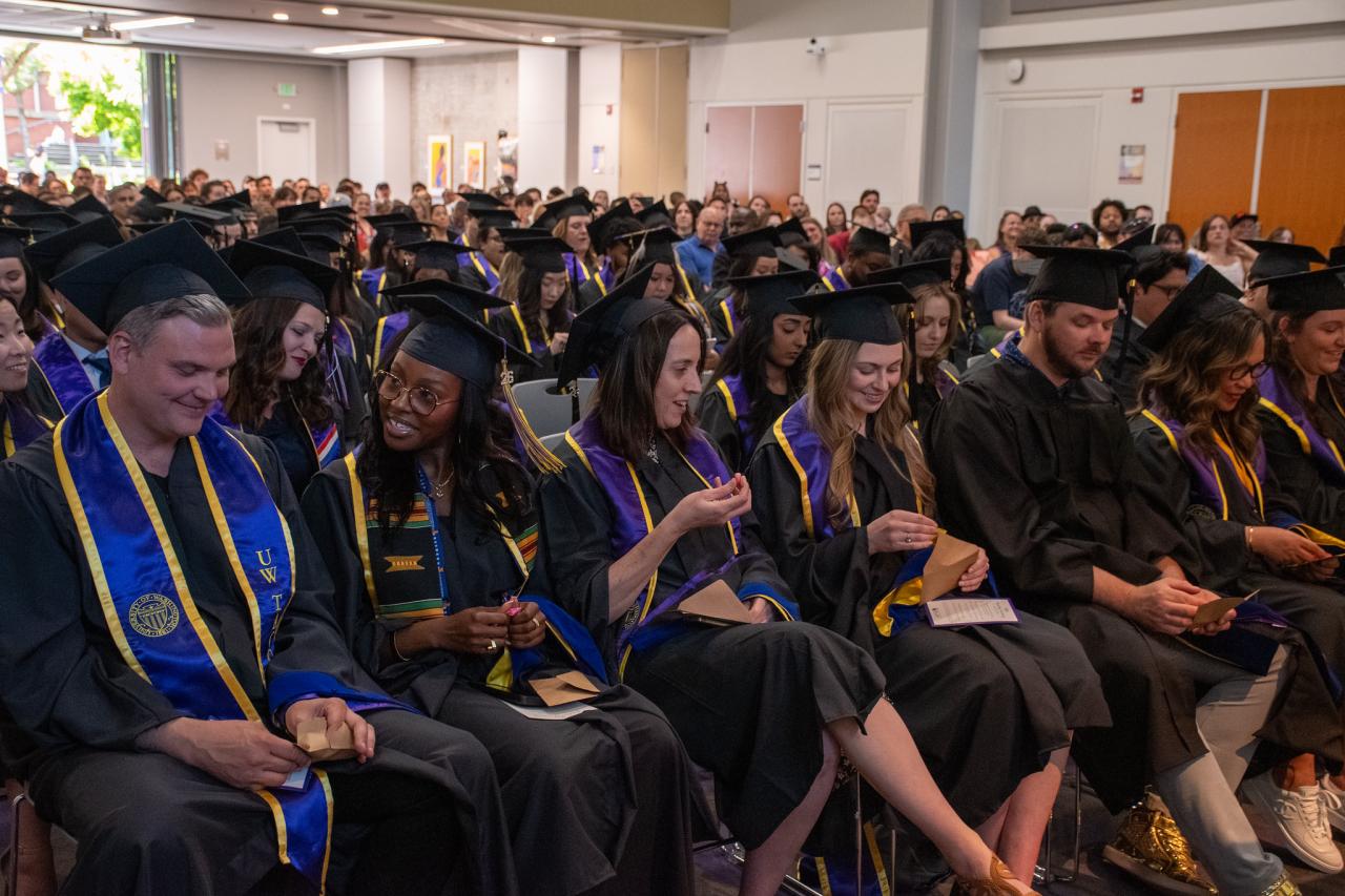 Graduating students wearing caps and gowns sitting in rows in an event space.