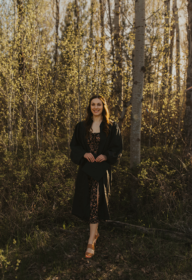 Photo of Michelle Crosby wearing graduation regalia in the woods