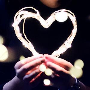 Two hands holding illuminated strings of lights shaped into a heart