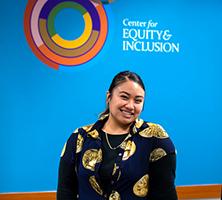 Nedralani Mailo standing under the logo of the UW Tacoma Center for Equity & Inclusion.