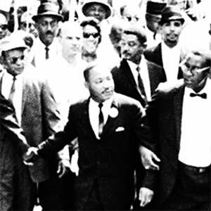 Black-and-white archival photo of Rev. Dr. Martin Luther King Jr. leading a protest march.