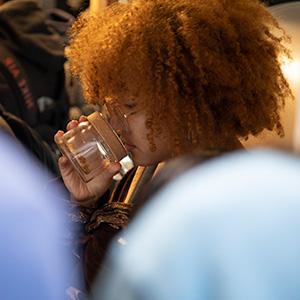 UW Tacoma student Elena Mendoza has her nose inside a jar of coffee beans. She has bright hair and wears glasses.