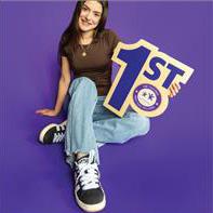A student holding a "1st" cut-out sign in front of a purple backdrop.