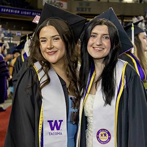 A photo of two UW Tacoma graduates smiling at the university's Commencement ceremony at the Tacoma Dome.