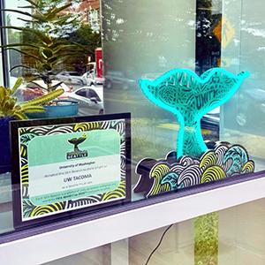 A "SEA Beacon" sculpture in the shape of a whale tail is on display in the front window of UW Tacoma’s University YMCA Student Center during the 2026 FIFA World Cup.