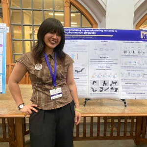 A student standing in front of their research poster presentation at the 2026 Undergraduate Research Symposium in Mary Gates Hall