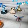 Close up picture of figurines from Dungeons & Dragons. There is a solider with a helmet and sword as well as a creature that resembles a fly. There are other creatures, one blue and one multicolored. In the background are out of focus blue dice.