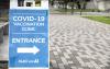 Blue and white sign standing on white and grey pavers, announcing COVID-19 vaccination clinic sponsored by MultiCare