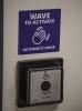 Purple and white sign with instructions "Wave to activate" above square door-opening sensor device