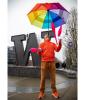 Alex Zerbe, wearing orange jacket, with rainbow-colored umbrella balanced on chin, juggling pins in front of W Tacoma sign.