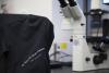 The shoulder of Dr. Anna Groat Carmona's jacket with embroidered name, and a lab microscope in background.