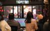 A group of people stand behind a window and look out over the stage at the Tacoma Little Theatre. The people are audio engineers for the show and are checking sound levels.