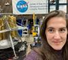 UW Tacoma mechanical engineering student Amy Keller at NASA Langley Research Center near her workspace, with an Artemis lander concept to left and her tower project behind her.