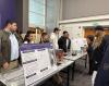 6 students standing behind 2 posters, presenting their research to guests