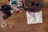 on a table the following things laid out: phone, camera, scarf, sunglass, bag, and shirt