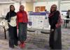 Photo of 3 students standing in front of a poster board, smiling for the camera