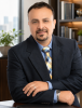 Photo of man leaning against desk with bookshelf and city skyline in background