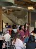 Students sit and stand around small tables inside of an industrial lobby talking to each other.